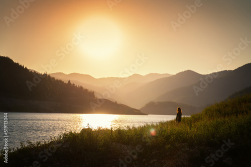 Woman traveler admiring the sunset on the shore of a lake in the mountains. Tara National Park, travel to Serbia