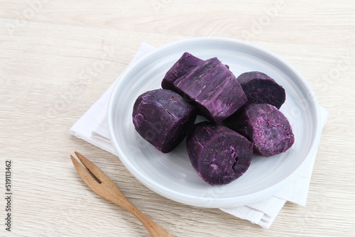 Steamed Purple Sweet Potato (Ubi ungu kukus) served in white plate on wooden table. 
