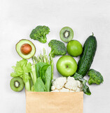 paper bag with green vegetables and fruits on a gray concrete background