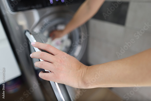 Woman hand fills drum of washing machine closeup