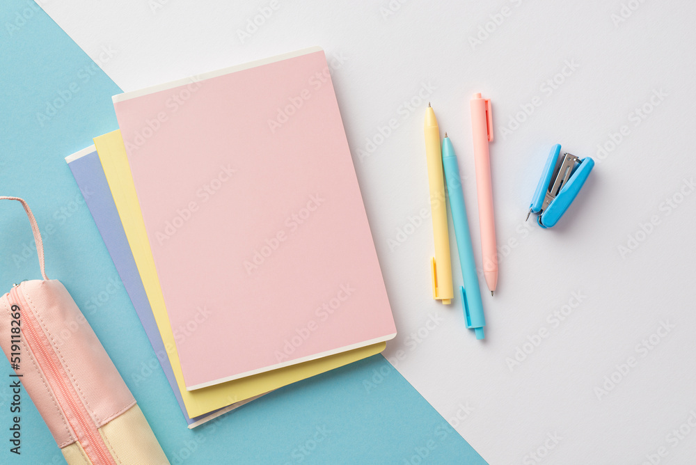 Back to school concept. Top view photo of colorful school supplies stack of copybooks pens mini stapler and pink pencil-case on bicolor blue and white background Back to school concept. Top view photo of colorful school supplies stack of copybooks pens mini stapler and pink pencil-case on bicolor blue and white background