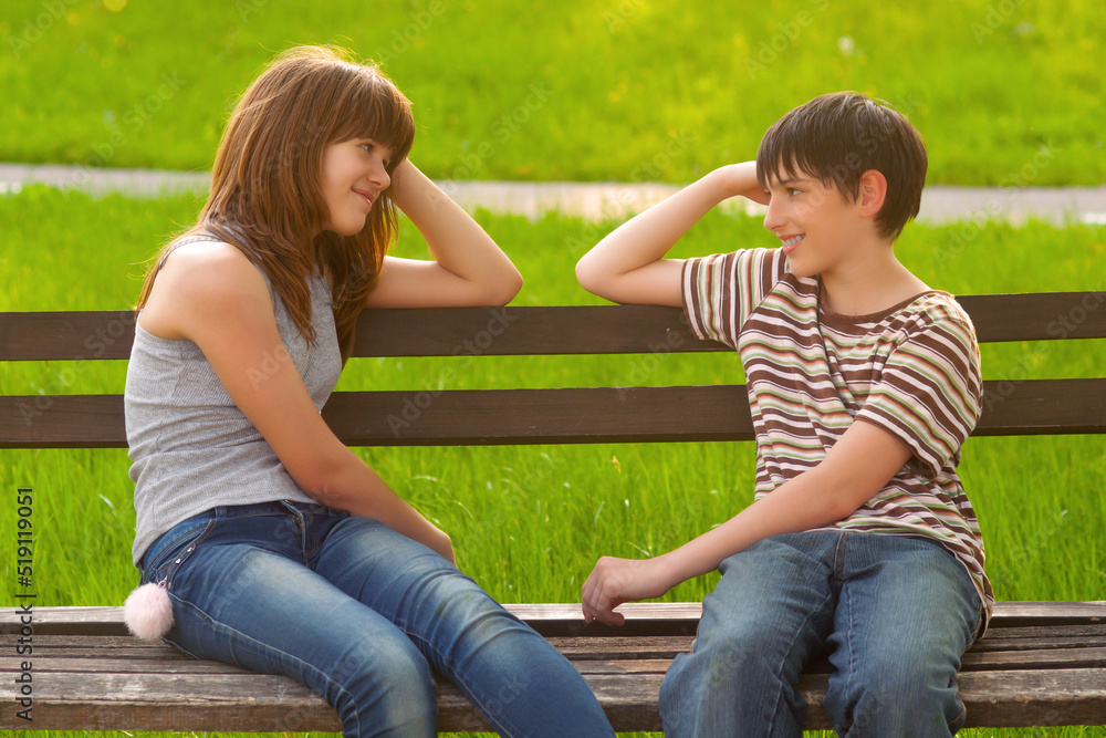 Fototapeta premium Smiling teenage boy and girl sitting on the bench in the summer park 