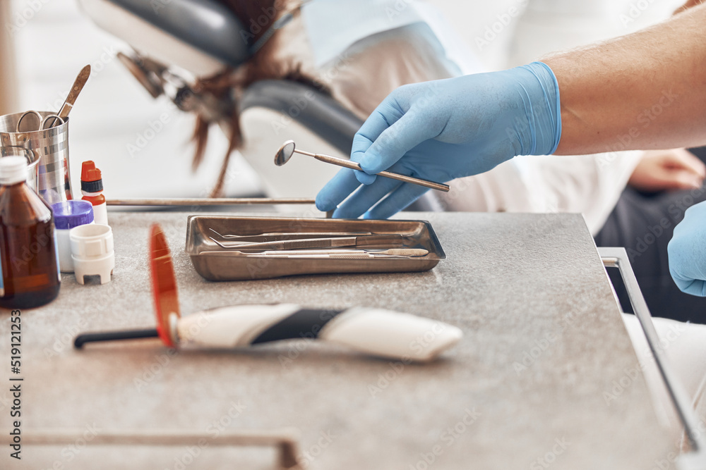 Hand in glove is holding dentist instrument in white modern cabinet Hand in glove is holding dentist instrument in white modern cabinet