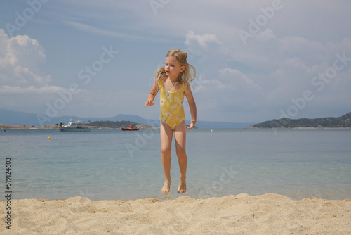 Cheerful little 4 years old girl playing and jumping on the sand beach