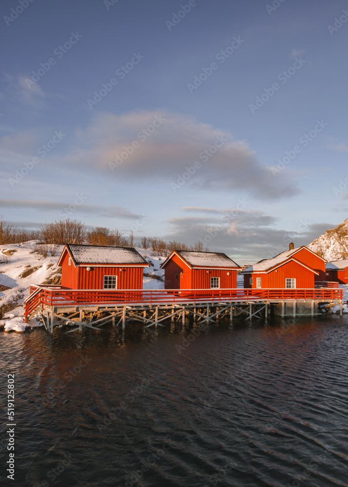 Famous red rorbuers of Lofoten near the Artic sea. Sunset light at winter, the isolated village is covered by snow.