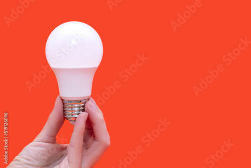 Energy saving light bulb in hand on orange background with free space for text. Saving energy in everyday life. Electrical equipment and the evolution of light. Free space for text