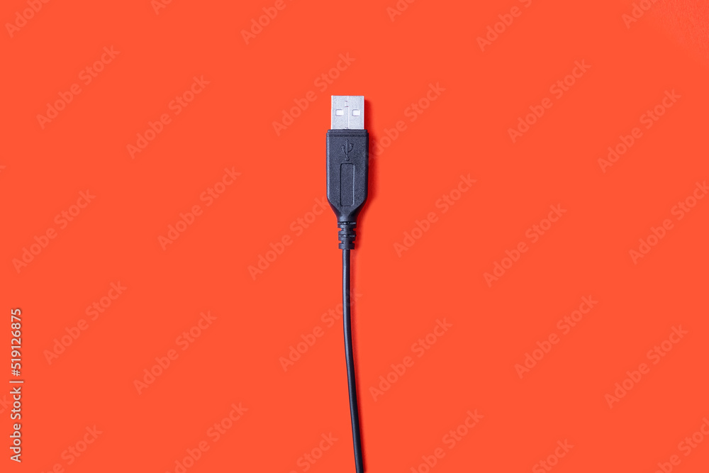 Black USB cable on an orange background in the center of the image. Modern technologies in everyday life. Compatible with many electronic devices. Cable for digital information transmission Black USB cable on an orange background in the center of the image. Modern technologies in everyday life. Compatible with many electronic devices. Cable for digital information transmission