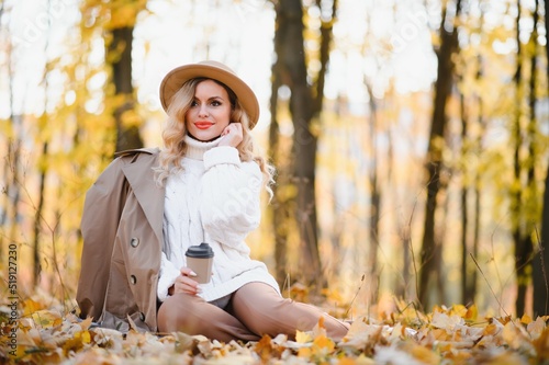 Young beautiful woman holding cup with coffee in the autumn park.
