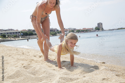 Mother and daughter playing on beach, exercising for a wheelbarrow race. photo