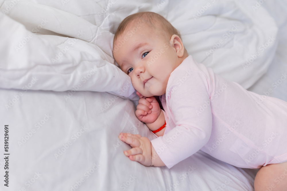 baby in a pink bodysuit is lying in a crib on snow-white bed linen, lifestyle baby in a pink bodysuit is lying in a crib on snow-white bed linen, lifestyle