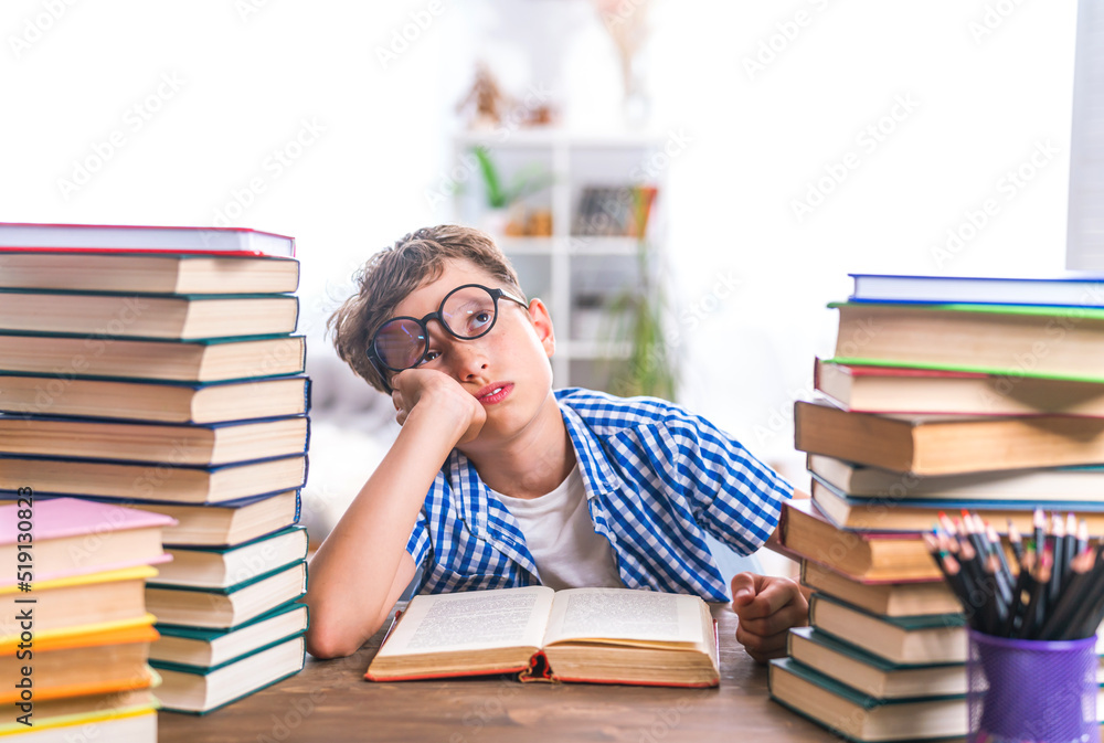 schoolboy tired of learning, wearing glasses, doing homework, sitting indoors between stacks of books. child falls asleep from boredom, does not want to study. no motivation. Problems with learning. schoolboy tired of learning, wearing glasses, doing homework, sitting indoors between stacks of books. child falls asleep from boredom, does not want to study. no motivation. Problems with learning.