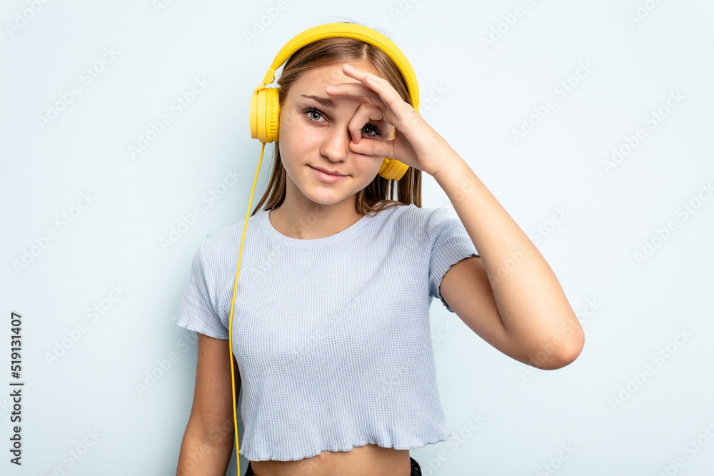 Young caucasian girl listening to music isolated on blue background excited keeping ok gesture on eye.
