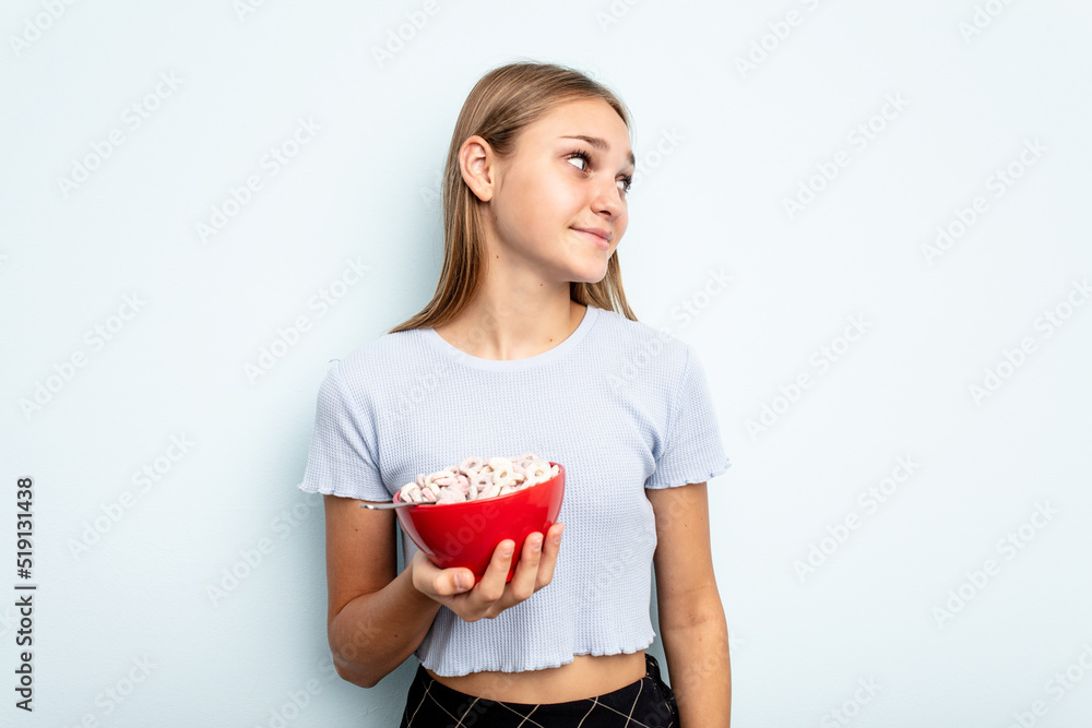Young caucasian girl eating cereals isolated on blue background dreaming of achieving goals and purposes