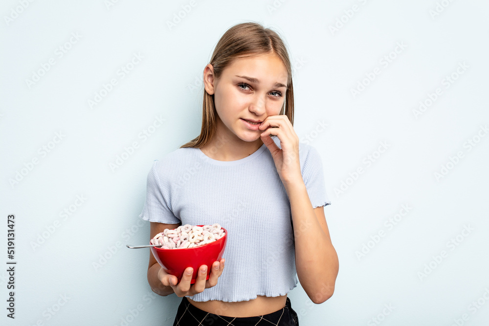 Young caucasian girl eating cereals isolated on blue background biting fingernails, nervous and very anxious. Young caucasian girl eating cereals isolated on blue background biting fingernails, nervous and very anxious.