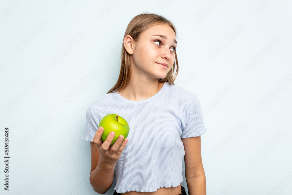 Young caucasian girl holding an apple isolated on blue background dreaming of achieving goals and purposes Young caucasian girl holding an apple isolated on blue background dreaming of achieving goals and purposes
