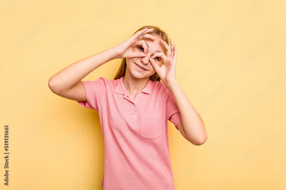 Young caucasian girl isolated on yellow background showing okay sign over eyes Young caucasian girl isolated on yellow background showing okay sign over eyes