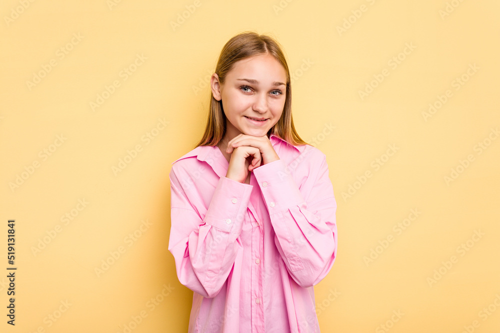 Young caucasian girl isolated on yellow background keeps hands under chin, is looking happily aside. Young caucasian girl isolated on yellow background keeps hands under chin, is looking happily aside.