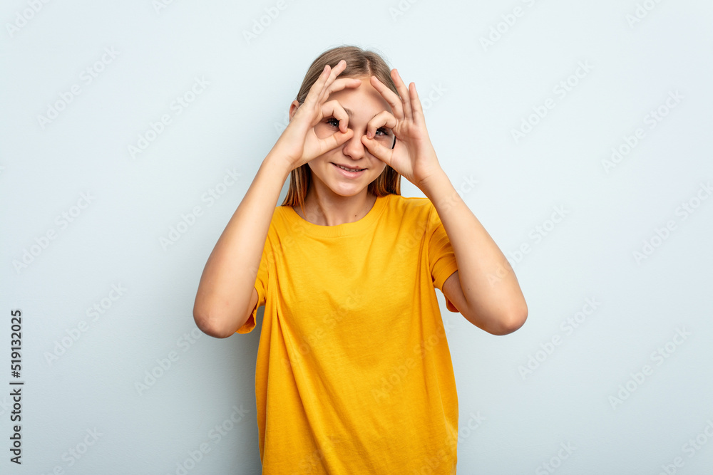 Young caucasian girl isolated on blue background showing okay sign over eyes Young caucasian girl isolated on blue background showing okay sign over eyes