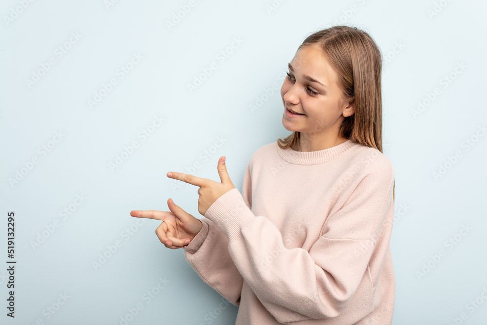 Young caucasian girl isolated on blue background points with thumb finger away, laughing and carefree.