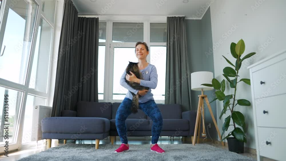 Woman squats with a cat in her arms, slow motion. Home workouts. Woman squats with a cat in her arms, slow motion. Home workouts.