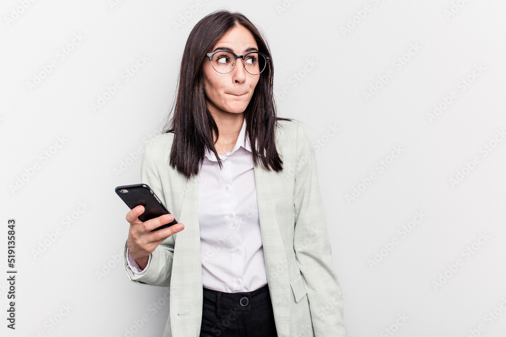 Young business caucasian woman holding mobile phone isolated on white background confused, feels doubtful and unsure. Young business caucasian woman holding mobile phone isolated on white background confused, feels doubtful and unsure.