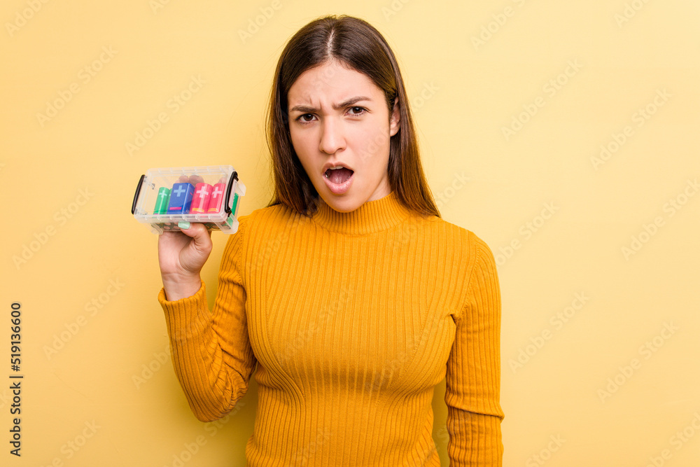 Young caucasian woman holding a batteries box isolated on yellow background screaming very angry and aggressive.