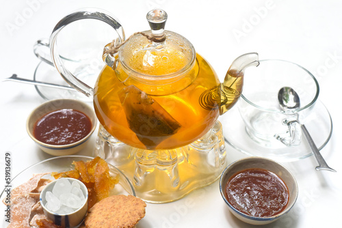 Glass tea pot with cups marmalade and crystalized fruits on white background