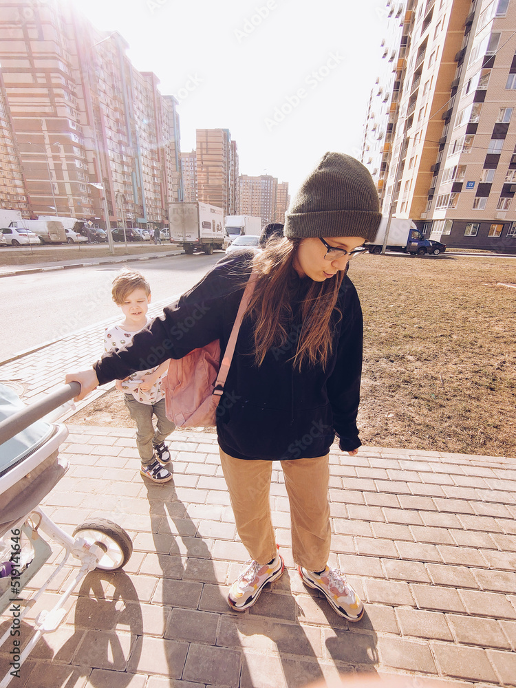 Millennial mother walking around the town with a baby stroller with older son near.Living with kids, fresh air, leisure activity, healthy lifestyle, daily routine, love and care, motherhood, childhood