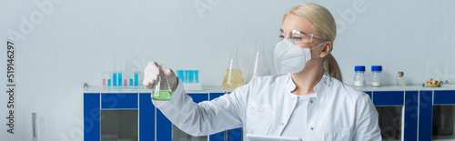 Scientist in white coat holding flask and digital tablet in lab  banner.