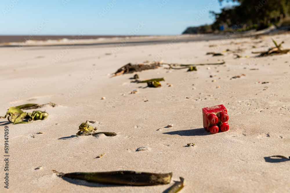 A children's toy for construction by blocks, red in color, thrown in the sand as garbage and pollution that the sea took out on the beach A children's toy for construction by blocks, red in color, thrown in the sand as garbage and pollution that the sea took out on the beach