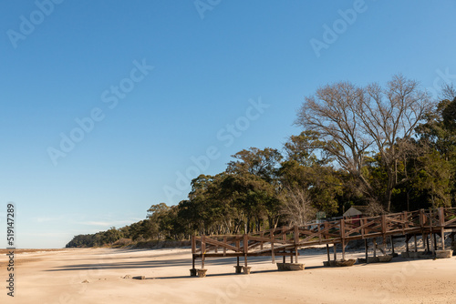 Fototapeta Naklejka Na Ścianę i Meble -  Old pier, now deck, on the sands of Kiyu beach, with the trees on the ravines of the coast, in San Jose, Uruguay