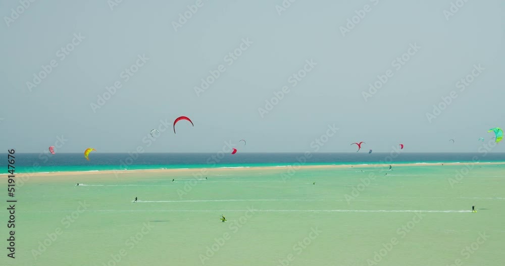 Kitesurfing on the tropical beach of Playa Del Mal Nombre, Fuerteventura, Canary Islands. People engaged in kiteboarding turquoise sea. The men on the board swims fast on the waves in shallow water. Kitesurfing on the tropical beach of Playa Del Mal Nombre, Fuerteventura, Canary Islands. People engaged in kiteboarding turquoise sea. The men on the board swims fast on the waves in shallow water.