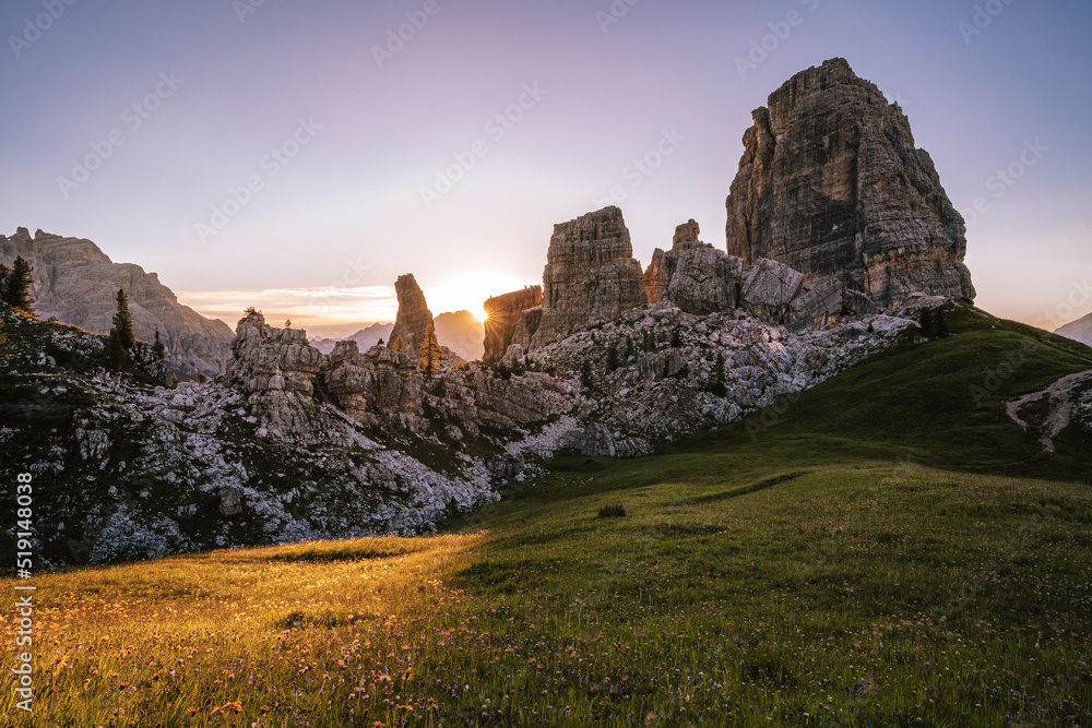 Sunrise at famous rock towers of Cinque Torri, Cortina D'Ampezzo, Dolomites, Italy. Summer mountain sunrise with sun peaking behind alpine landscape.