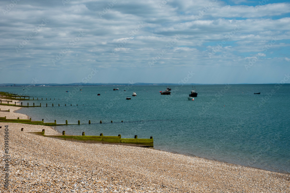 deserted pebble beach at Selsey West Sussex England with fishing boats in the background