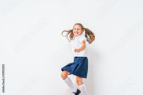 happy schoolgirl in a school uniform, jumping on a white background in the studio. the little girl is ready for school conceptual school. the holidays begin. Advertising discounts