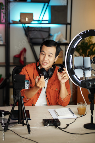 Young Asian tech blogger filming earbuds review for social media photo