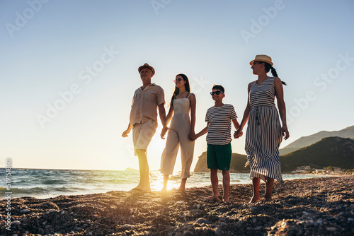 Family holding hands enjoying the sunset on the beach. Happy family travel and vacations concept.