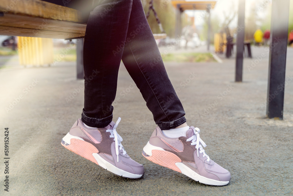 cropped image of female legs in shoes. Woman in green sweatshirt and black jeans sits on swing. Womens legs in pink sneakers cropped image of female legs in shoes. Woman in green sweatshirt and black jeans sits on swing. Womens legs in pink sneakers
