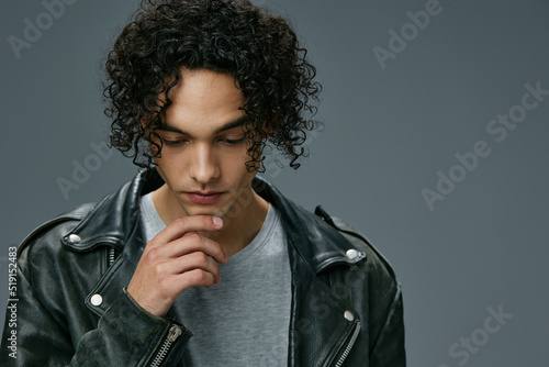 Close up headshot portrait of stylish tanned curly man leather jacket posing isolated on over gray studio background. Cool fashion offer. Huge Seasonal Sale New Collection concept. Copy space for ad