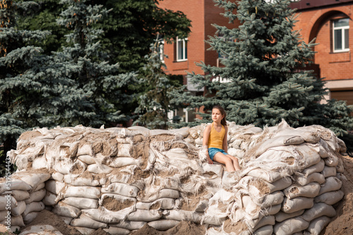 Wallpaper Mural War in Ukraine. A girl sits on sandbags near her house. This building was made for the defense of the city. Life during the war. Torontodigital.ca