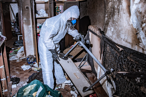 a specialist in a protective suit from a cleaning company cleans a destroyed housing after a fire