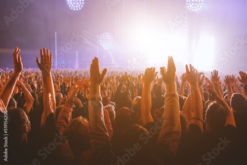 Performance of a popular group. The crowd with raised hands against the stage light.