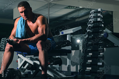 Shirtless sportsman resting after training at the gym. Portrait of athletic man with dumbbells. Shirtless man man with muscles torso, in the gym. photo