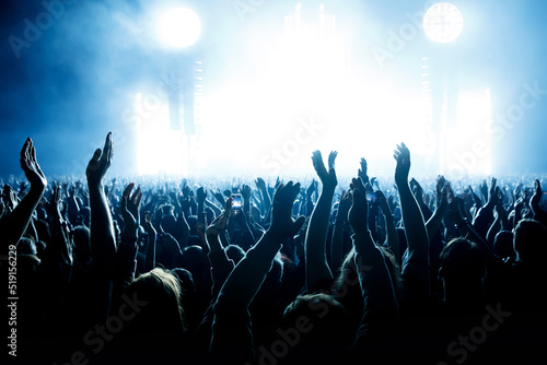Performance of a popular group. The crowd with raised hands against the stage light.