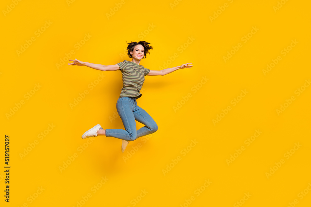 Full length photo of pretty adorable girl dressed green t-shirt jumping high empty space isolated yellow color background