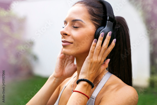 Closeup shot of beautiful young woman with headphones with her eyes closed, relaxing music, relaxing in the garden 