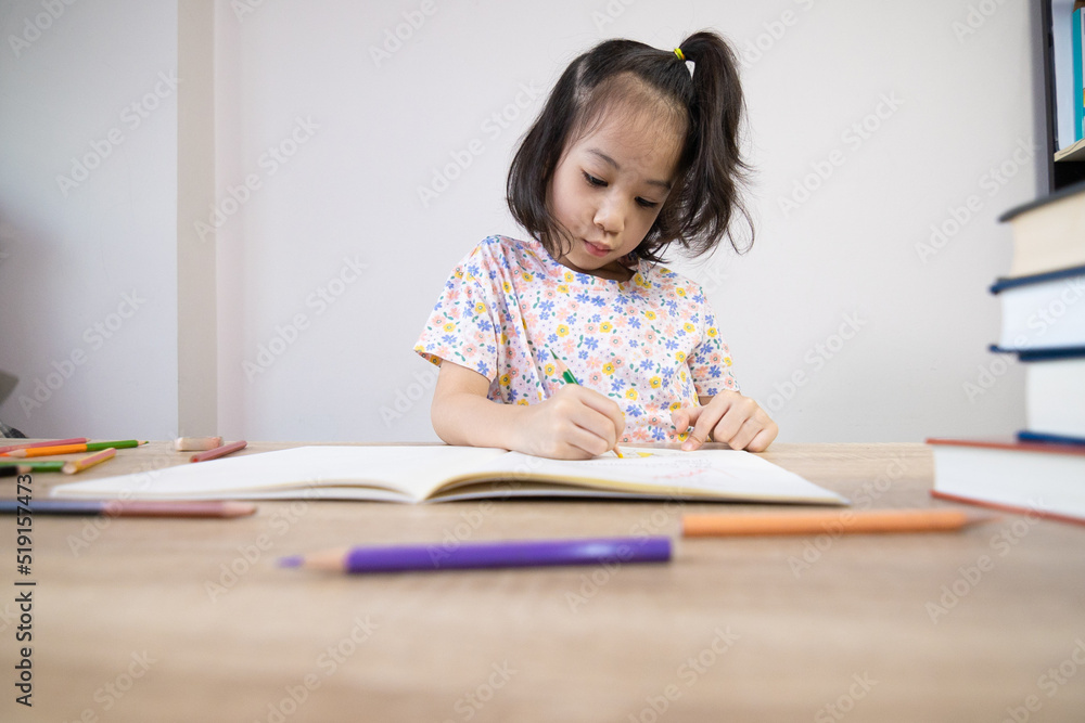 Adorable asian girl is doing her homework on the table with a lot of books and pencil. It shows concept of smart and clever child learning by herself to gain knowledge which is basic education. Adorable asian girl is doing her homework on the table with a lot of books and pencil. It shows concept of smart and clever child learning by herself to gain knowledge which is basic education.