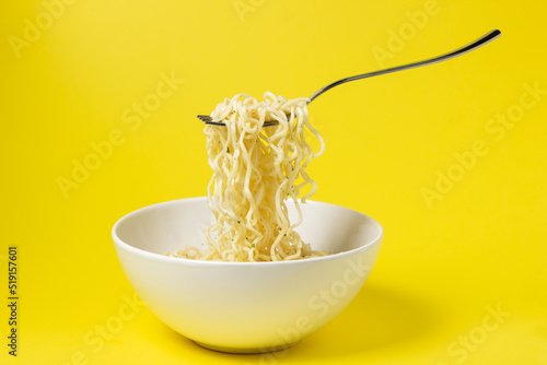 Boiled instant noodles on a yellow background. Fork with noodles in the air. Fast food. Modern food. photo