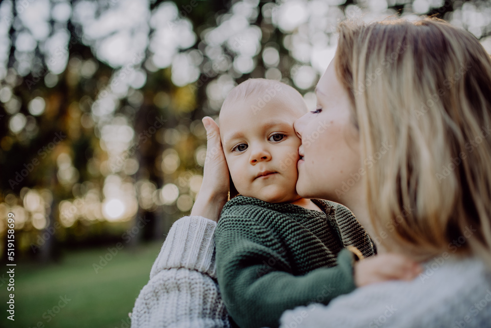Obraz premium Mother holding and kissing her little baby son wearing knitted sweater during walk in nature, close-up
