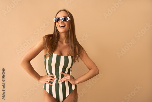  A stylish tanned woman on a beige background is smiling.